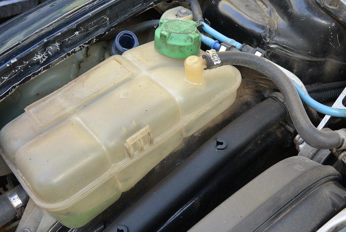 A translucent coolant expansion tank with a green filler cap, under the bonnet of a car