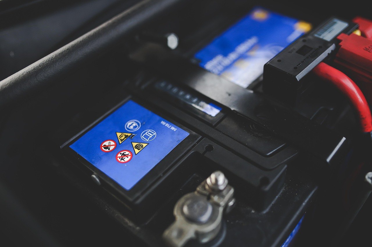 Close-up of a car battery, showing the warning symbols on its label and one of its terminal clamps