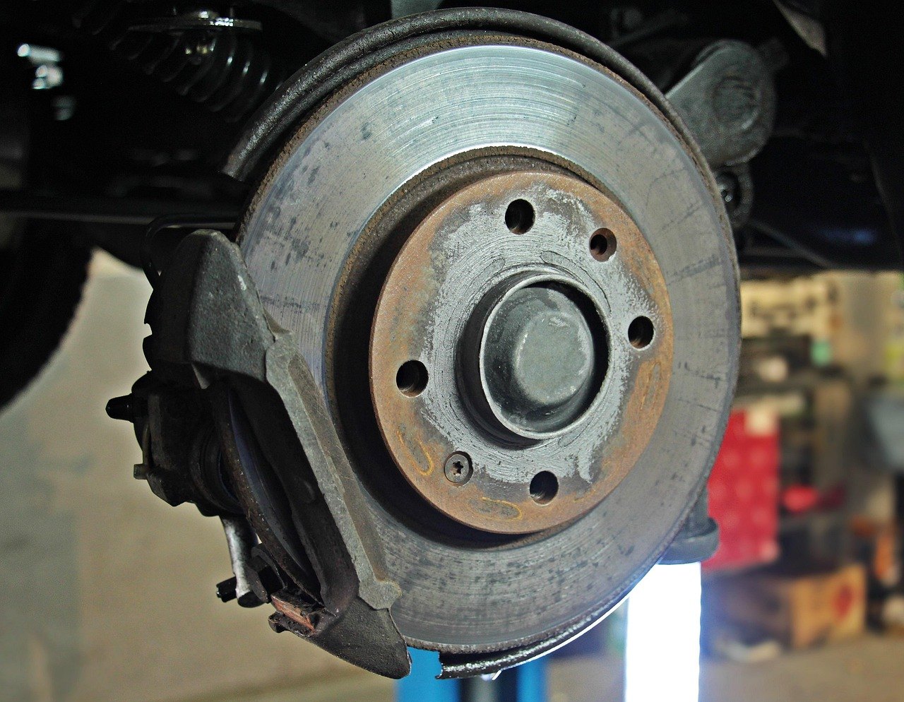 A brake disc and its caliper on a car raised in a workshop, with the wheel removed